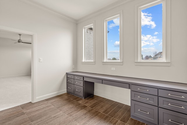 unfurnished office featuring ornamental molding, built in desk, a ceiling fan, and baseboards