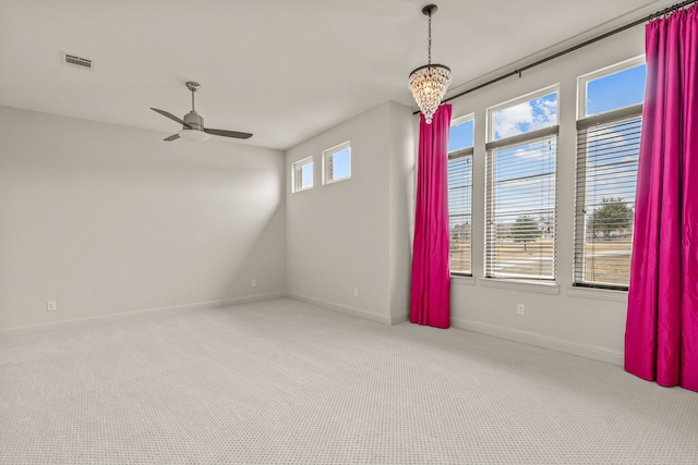 empty room with ceiling fan with notable chandelier, carpet flooring, visible vents, and baseboards