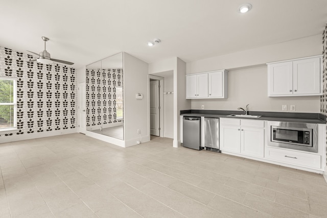 kitchen featuring a ceiling fan, dark countertops, stainless steel microwave, white cabinetry, and a sink