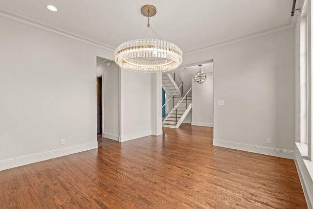 empty room with crown molding, an inviting chandelier, wood finished floors, baseboards, and stairs