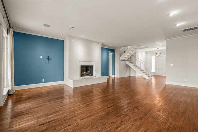 unfurnished living room with a fireplace with raised hearth, wood finished floors, visible vents, stairway, and crown molding