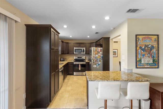 kitchen featuring dark brown cabinetry, visible vents, a peninsula, light stone countertops, and stainless steel appliances