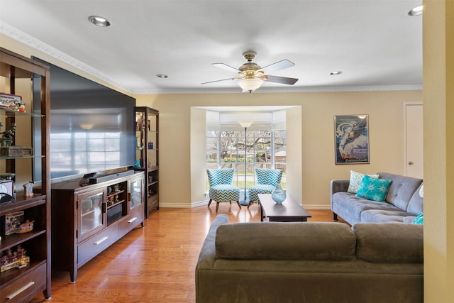 living area featuring light wood-style floors, ornamental molding, baseboards, and ceiling fan