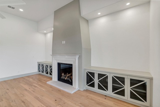 unfurnished living room with wood finished floors, a glass covered fireplace, visible vents, and recessed lighting