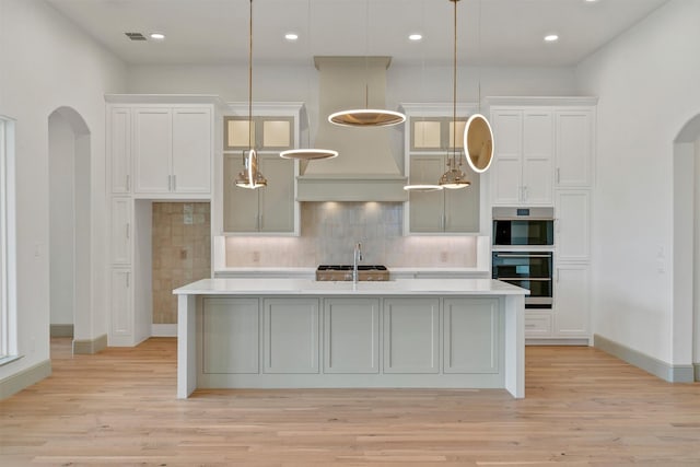 kitchen with arched walkways, decorative backsplash, white cabinets, an island with sink, and light countertops