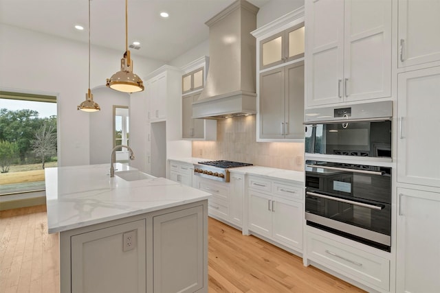 kitchen featuring tasteful backsplash, wall chimney exhaust hood, stainless steel double oven, gas cooktop, and a sink