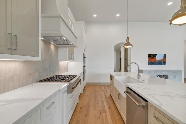 kitchen featuring stainless steel appliances, backsplash, a sink, light wood-type flooring, and premium range hood