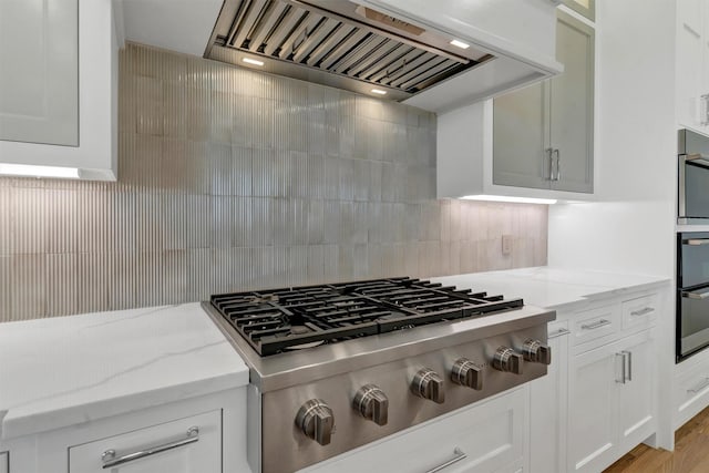 kitchen with stainless steel gas cooktop, white cabinets, light stone countertops, tasteful backsplash, and custom range hood