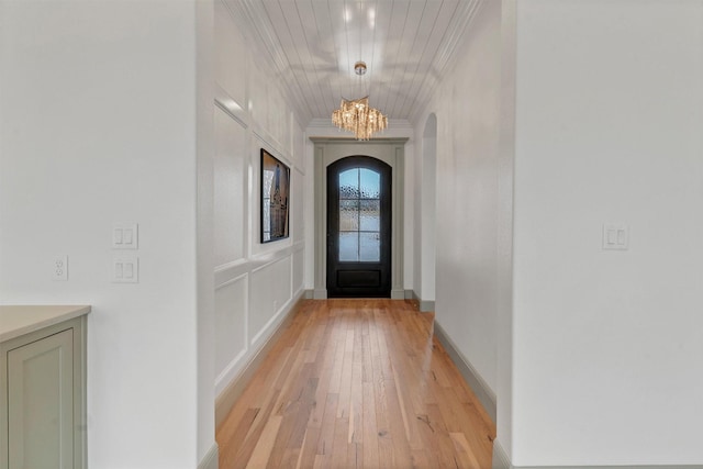 entryway featuring a chandelier, arched walkways, light wood-style floors, baseboards, and crown molding