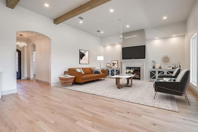 living area with visible vents, arched walkways, a glass covered fireplace, wood finished floors, and beam ceiling