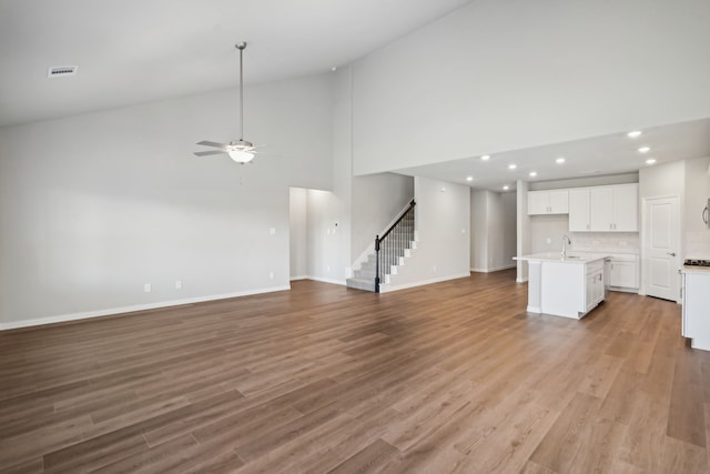 unfurnished living room with visible vents, ceiling fan, a sink, light wood-type flooring, and stairs