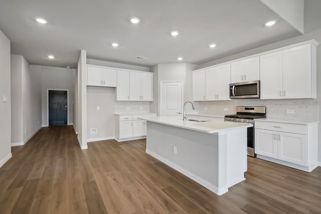 kitchen with dark wood-style flooring, a sink, white cabinetry, appliances with stainless steel finishes, and a center island with sink