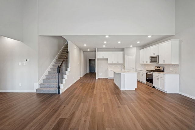 kitchen with an island with sink, appliances with stainless steel finishes, wood finished floors, white cabinetry, and backsplash