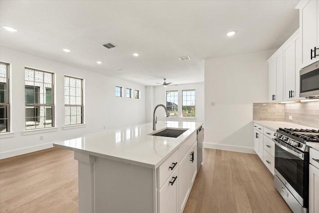 kitchen featuring stainless steel appliances, decorative backsplash, a sink, an island with sink, and light wood-type flooring