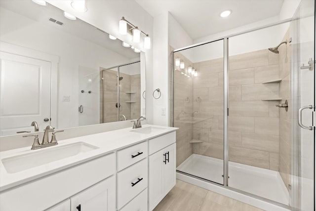 bathroom with visible vents, a sink, a shower stall, and double vanity