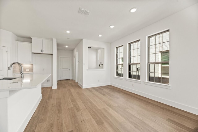 unfurnished living room featuring recessed lighting, a sink, visible vents, baseboards, and light wood-style floors