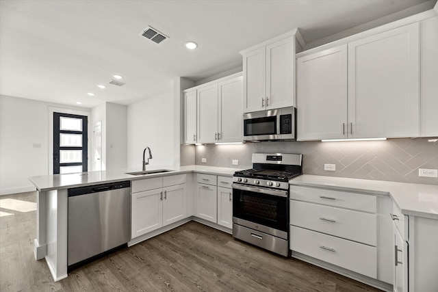 kitchen with a peninsula, dark wood-style flooring, a sink, visible vents, and appliances with stainless steel finishes