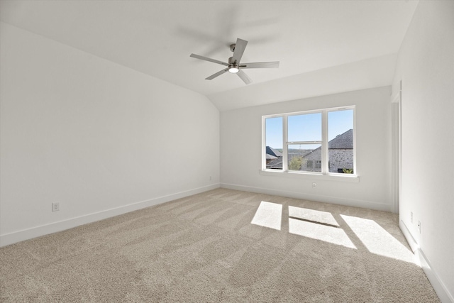 spare room featuring vaulted ceiling, light carpet, a ceiling fan, and baseboards