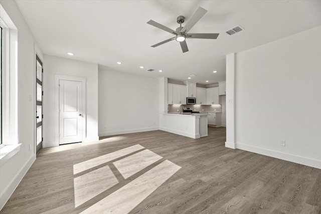 unfurnished living room with light wood finished floors, visible vents, and baseboards