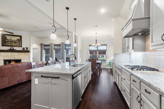 kitchen with appliances with stainless steel finishes, ornamental molding, custom exhaust hood, a stone fireplace, and a sink