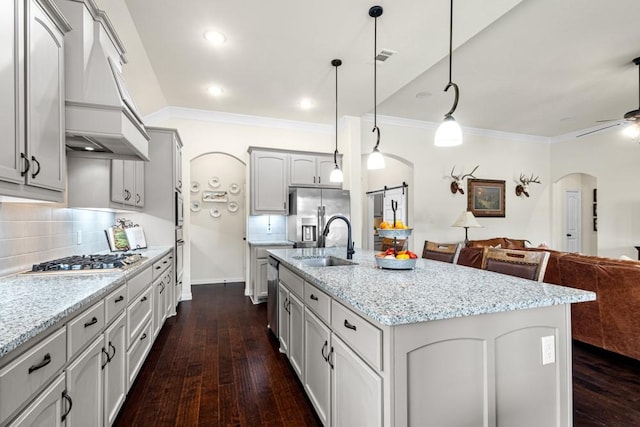 kitchen featuring arched walkways, stainless steel appliances, open floor plan, a sink, and premium range hood