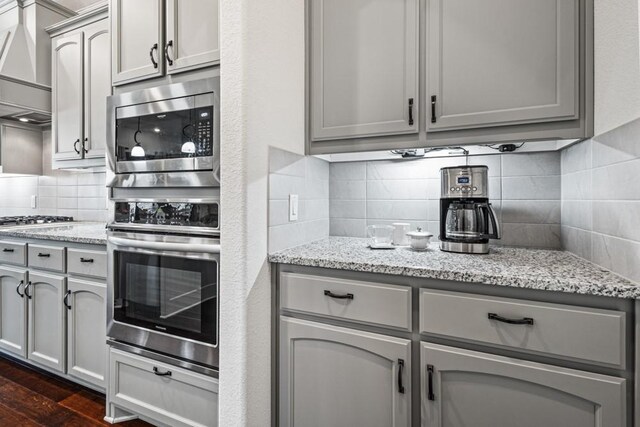 kitchen featuring dark wood-style floors, tasteful backsplash, gray cabinetry, appliances with stainless steel finishes, and wall chimney exhaust hood