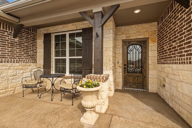 doorway to property featuring a porch, stone siding, and brick siding