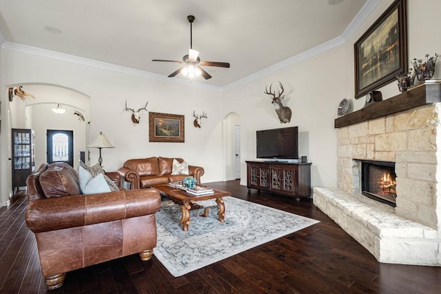 living room featuring arched walkways, a fireplace, a ceiling fan, ornamental molding, and hardwood / wood-style floors