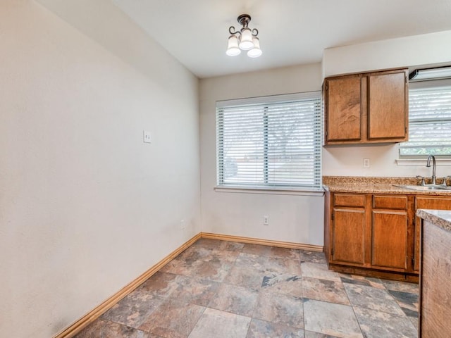 kitchen featuring light countertops, brown cabinetry, stone finish floor, a sink, and baseboards