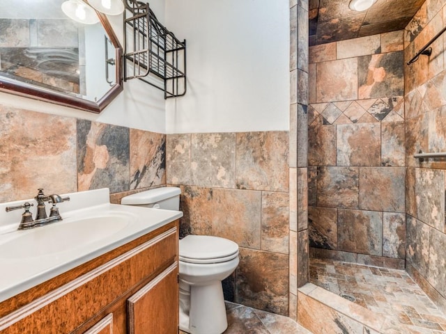 bathroom with tile walls, toilet, wainscoting, vanity, and tiled shower