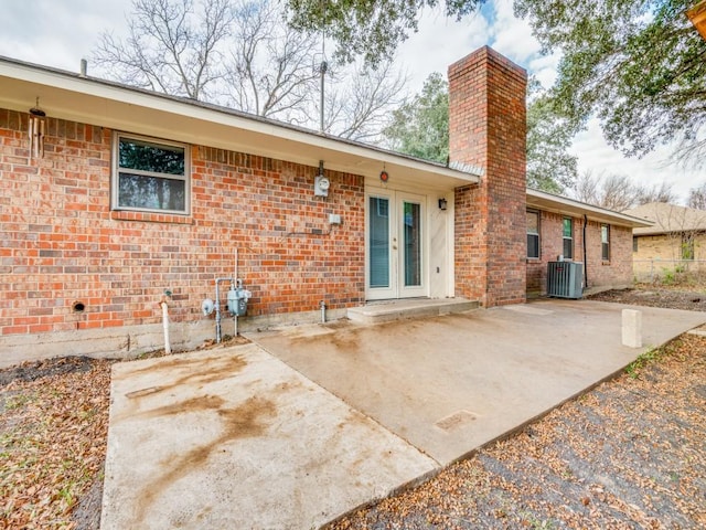 rear view of house featuring french doors, brick siding, a chimney, and cooling unit