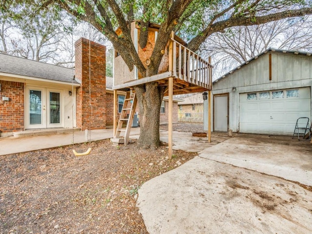 exterior space with a chimney, french doors, concrete driveway, and brick siding