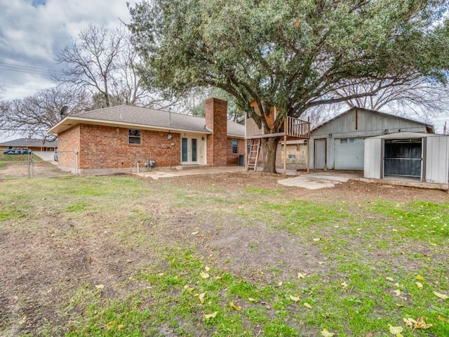 back of house featuring brick siding, an outdoor structure, fence, french doors, and a chimney