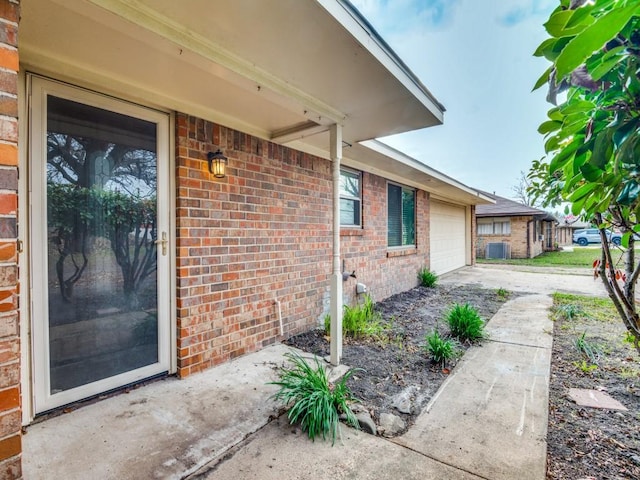 doorway to property featuring a garage, concrete driveway, and brick siding