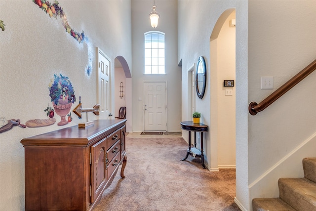 foyer entrance featuring arched walkways, light colored carpet, a towering ceiling, baseboards, and stairs