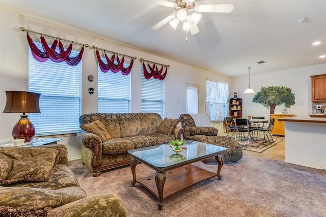 living room featuring light carpet, visible vents, a ceiling fan, and light tile patterned flooring