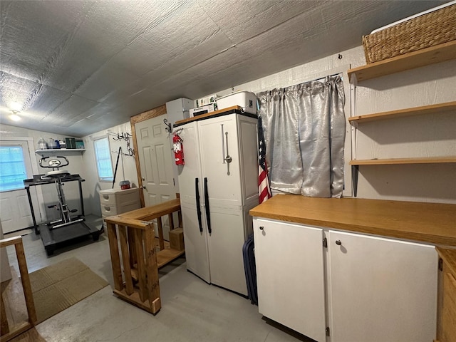 interior space featuring vaulted ceiling, open shelves, concrete floors, and white cabinets