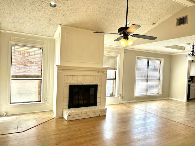 unfurnished living room featuring a textured ceiling, visible vents, ornamental molding, light wood-type flooring, and a brick fireplace