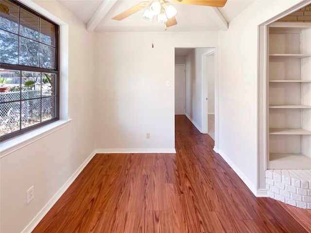 empty room with a ceiling fan, beam ceiling, baseboards, and wood finished floors