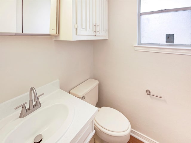 half bathroom featuring toilet, baseboards, and vanity