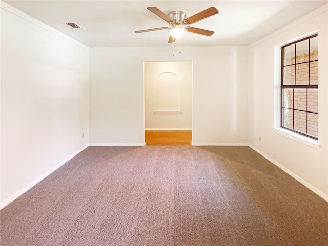 carpeted spare room with visible vents, crown molding, baseboards, and ceiling fan