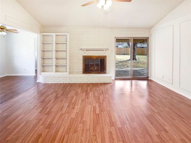 unfurnished living room featuring ceiling fan, a fireplace, wood finished floors, built in features, and vaulted ceiling