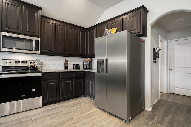 kitchen featuring arched walkways, light stone counters, stainless steel appliances, decorative backsplash, and wood tiled floor