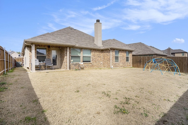 back of house featuring a shingled roof, a patio, a fenced backyard, a chimney, and brick siding