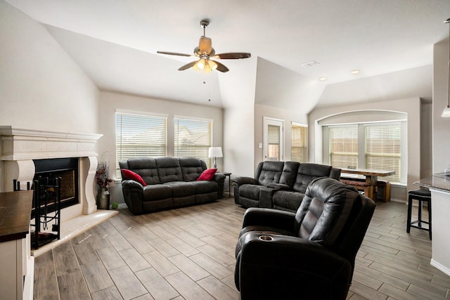 living area with visible vents, a fireplace with raised hearth, a ceiling fan, lofted ceiling, and wood finish floors