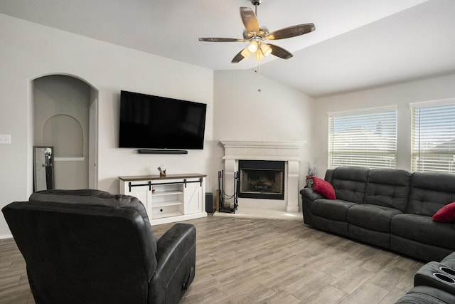 living area featuring lofted ceiling, a ceiling fan, a fireplace with raised hearth, and wood finished floors