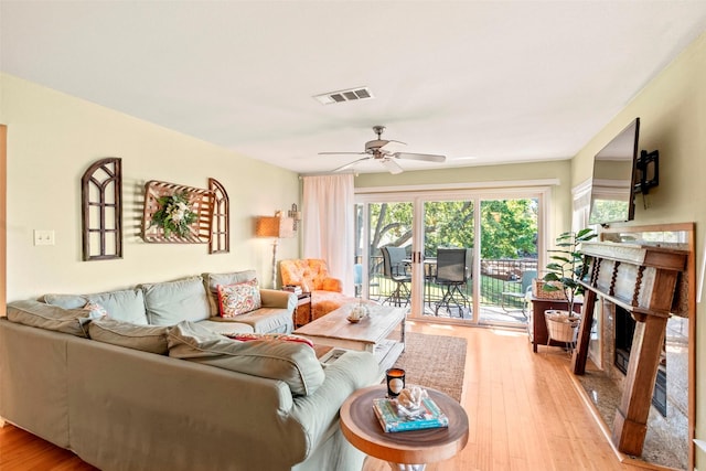 living room featuring a ceiling fan, visible vents, a fireplace, and light wood-style flooring