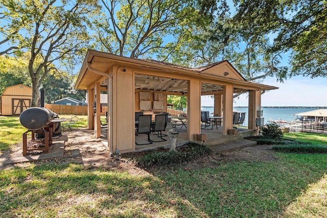 view of patio featuring fence, a storage shed, a gazebo, a water view, and an outbuilding