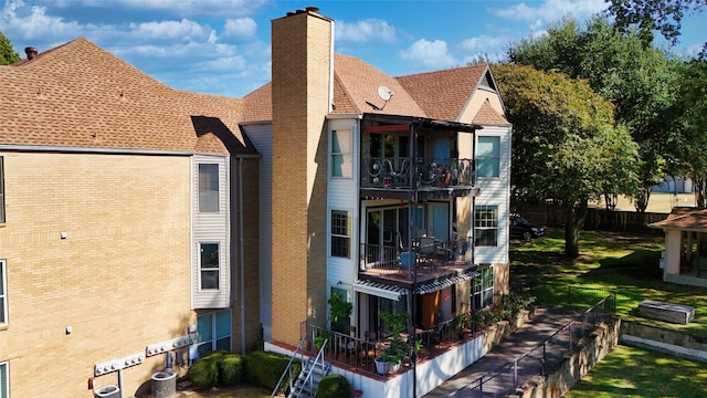 rear view of property featuring a chimney, brick siding, central AC, fence, and a balcony