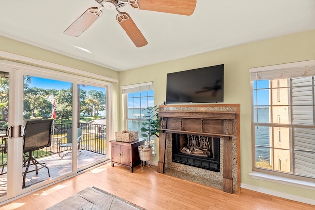 living area with a fireplace with flush hearth, ceiling fan, baseboards, and wood finished floors